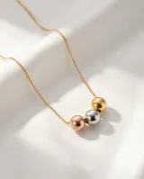 Collar de acero con cadena fina y tres dijes centrales en forma de esferas con acabados en plateado, dorado y oro rosa.