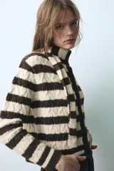 Chaqueta de punto a rayas horizontales en color marrón y beige, con cuello redondo, manga larga y cierre frontal con botones. Incluye una bufanda integrada del mismo tejido y diseño.