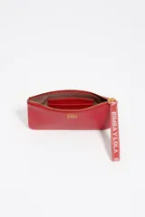 Monedero grande de piel vacuna color rojo, con cierre superior y correa de muñeca de tela con el logo de la marca. Incluye el logo metálico dorado en el frente.