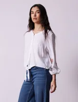 Blusa blanca de algodón marca Dash, con escote en V, abertura con botones, mangas 3/4 regulables con presilla y botón, y terminación de ruedo anudado.