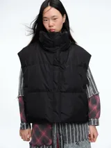 Chaleco puffer negro con cuello alto, cierre frontal oculto y diseño acolchado horizontal.