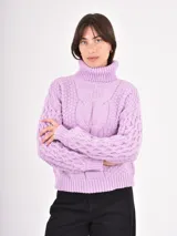 Polera de tejido de punto color lila, con cuello alto doblado y diseño de trenzas en el frente y las mangas. Presenta puños y ruedo acanalados.
