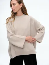 Sweater de tejido de punto en color beige, con cuello redondo y mangas anchas. Presenta un diseño con cortes laterales que aportan una estética contemporánea y una silueta holgada.