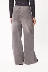 Jean wide leg de tiro medio con efecto lavado en color gris. Presenta un corte holgado de pierna ancha, cierre frontal con botón y cremallera, y bolsillos laterales. Incluye un pequeño bordado distintivo en la zona del bolsillo.