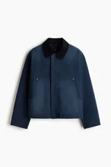 Campera worker corta de sarga de algodón en color azul oscuro, con cuello de pana negro en contraste. Cuenta con cierre frontal oculto por solapa con botones a presión y grandes bolsillos frontales tipo parche.