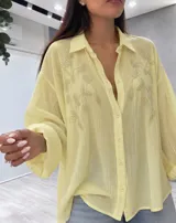 Camisa amarilla de manga larga con diseño oversize, cuello camisero y cierre frontal de botones. Presenta delicados bordados florales de abalorios y cuentas en el frente.