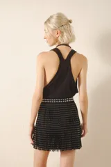 Falda corta negra de cuero con diseño de flecos y remaches metálicos plateados. La cintura es ancha y está adornada con tachas bombé.