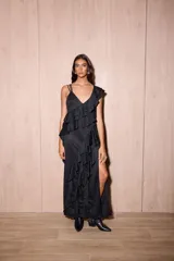 Vestido largo negro con volados verticales, tajo delantero, escote en V y finos tirantes cruzados en la espalda.
