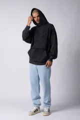 Buzo canguro de corte oversize, confeccionado en frisa de algodón con efecto de lavado gastado. Presenta un aplique decorativo cosido al corte en el centro del pecho, capucha amplia y bolsillo frontal tipo canguro.