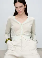 Cardigan de punto fino en color verde menta claro, con cuello en pico, cierre frontal de botones y diseño corto. Presenta mangas largas con puños elásticos y un acabado ligeramente traslúcido.
