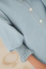 Vestido camisero de denim suave en tono celeste claro, con cuello mao, cierre frontal de botones y mangas tres cuartos con puños elásticos.