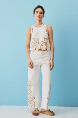 Blusa sin mangas de corte crop en color blanco, con detalles de bordados calados en tono tostado formando diseños florales en el cuello, los hombros y el borde inferior.