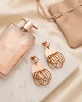 Caravanas colgantes de acero en tono rose gold, compuestas por un disco superior liso y una estructura inferior formada por múltiples aros entrelazados de textura trenzada.