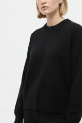 Sweater negro de punto liso, de corte holgado, con cuello redondo a la base y mangas largas.
