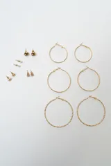 Set de siete pares de aros dorados de diversos estilos, incluyendo tres pares de aros tipo argolla de diferentes tamaños y texturas, y cuatro pares de aros pequeños con diseños variados como perlas, brillantes y formas geométricas.