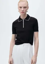 Jersey de punto fino color negro, con cuello polo y cierre frontal parcial. Presenta ribetes en contraste color blanco en el cuello y en los bordes de las mangas cortas.