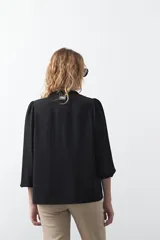 Camisa negra de corte clásico con escote en V, botones frontales y mangas largas con puños. Presenta detalles de recortes calados en la zona de los hombros.