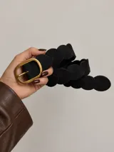Cinto negro de símil cuero con diseño trenzado en forma de pétalos y hebilla metálica dorada de estilo clásico.