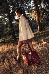 Cartera de cuero color bordó, tipo tote bag, con doble asa de hombro y hebillas decorativas a los costados. Incluye doble bolsillo y colgante interno para llaves.