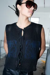 Chaleco de punto calado celeste con diseño estampado en negro y cierre frontal mediante tiras tejidas a crochet.
