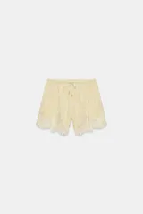 Shorts de tiro medio confeccionados en tejido jacquard con mezcla de cupro, en color beige. Presentan cintura elástica ajustable con cordones y detalle de aplicación de encaje a tono en el ruedo.