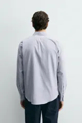 Camisa de corte regular fit confeccionada en tejido de algodón con diseño de rayas verticales. Presenta cuello abotonado, manga larga con puños abotonados y cierre frontal de botones.