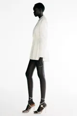 Blazer vestido corto confeccionado en tejido satinado color blanco, con cuello de solapa y cierre frontal cruzado con botones.