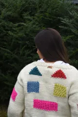 Cardigan de lana merino tejida a mano con dos agujas, color blanco con diseño de figuras geométricas en tonos multicolor y cierre frontal con botones de madera.