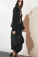 Top de manga larga negro, de tejido de punto semitransparente con efecto fruncido horizontal. Presenta cuello redondo con borde festoneado y cierre frontal con lazos finos.