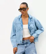 Campera de jean oversized de corte amplio con recortes estructurales, cierre frontal con botones metálicos, cuello clásico y bolsillos frontales.