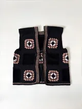 Chaleco sin mangas, confeccionado con cuadrados de cuero negro perforado combinados con cuadrados de crochet en hilo de algodón negro y blanco, con detalles centrales en rojo.