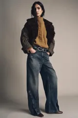 Jeans de mezclilla azul oscuro con efecto lavado, tiro medio y corte balloon (pierna ancha y holgada). Presenta cinco bolsillos y cremalleras metálicas decorativas que recorren la parte exterior de las piernas desde el muslo hasta el bajo.