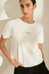 Remera color crudo con detalles de costuras marrones en contraste en el cuello, mangas y dobladillo, y el logo de la marca estampado en el pecho.