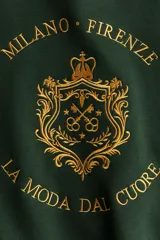 Buzo verde oscuro con cuello redondo, hombros caídos y un diseño frontal dorado que incluye una corona, un escudo y las palabras "Milano Firenze" y "La moda dal cuore". Tiene remates acanalados en cuello, puños y bajo, y un interior cepillado suave.