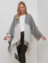 Ruana tejida con diseño colorblock en tonos de gris y beige, con flecos en el borde inferior.