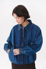 Campera de denim azul con corte oversized, cierre frontal y cuello de piel sintética marrón desmontable. Presenta detalles de volados en el frente, puños elásticos y logo bordado en el pecho.