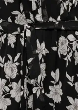 Vestido corto de poliéster con estampado floral en tonos blanco y negro. Presenta cuello redondo, mangas largas acampanadas, lazo ajustable en la cintura y bajo con volante.