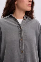 Camisa de jean de corte oversize y largo tipo túnica en color gris desgastado, con mangas largas, cuello camisero y cierre frontal de botones.