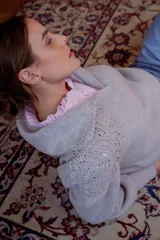 Sweater de punto color gris claro, con cuello amplio tipo solapa y detalles de tejido crochet en los hombros y mangas. Presenta mangas largas con puños ajustados y diseño de corte holgado.