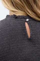 Blusa de color gris oscuro con diseño de punto smock en el cuerpo, cuello redondo y mangas cortas abullonadas con detalle de volados en el ruedo.
