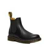 Bota Chelsea Dr. Martens modelo 2976, confeccionada en cuero liso negro con inserciones elásticas laterales, tirador en el talón y suela con cámara de aire reforzada con pespunte amarillo característico.
