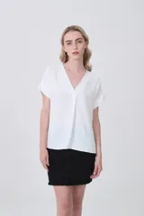 Blusa de poliéster color blanco con cuello en V, mangas cortas con dobladillo y corte holgado.
