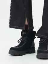 Borcegos de caña baja con diseño robusto, confeccionados en una combinación de gamuza y cuero sintético en tonos verde oliva. Presentan suela track de goma dentada en color suela, cordones al tono con ojalillos amarillos y cuello acolchado para mayor confort.