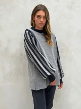 Sweater de lana color crudo con mangas largas abullonadas en gris y blanco, con diseño de rayas y perforaciones. Cuello redondo y puños acanalados.