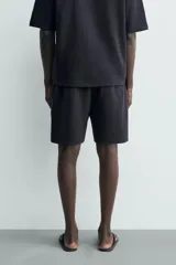 Bermuda estilo jogger de ajuste relajado, color negro, confeccionada en tejido interlock de algodón. Cuenta con cintura elástica ajustable mediante cordón, bolsillos delanteros tipo vivo y diseño liso.