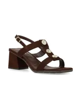 Sandalias de taco cuadrado en tono marrón chocolate, confeccionadas en gamuza. Poseen tiras cruzadas en el empeine con detalles de botones metálicos dorados decorativos, tira ajustable al talón con hebilla dorada y taco ancho estable.