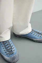 Zapatilla de cordones con diseño de inspiración montañista, confeccionada en piel con acabado de serraje en color azul. Presenta una puntera y refuerzo lateral en gamuza gris con textura desgastada, horma redonda y suela de goma dentada VIBRAM®.