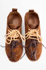 Championes urbanos de cuero vacuno en color marrón, con diseño de paneles superpuestos y costuras decorativas en zigzag. Presenta cordones bicolores y suela de goma al tono.