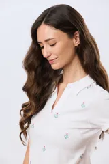 Remera polo de algodón color beige con mangas cortas, escote en V y cuello camisero. Presenta delicados mini bordados florales distribuidos en toda la prenda.