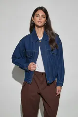 Campera de jean azul oscuro, de corte oversize, con cuello clásico, cierre frontal con cremallera y botones a presión, bolsillos frontales con solapa y mangas largas.